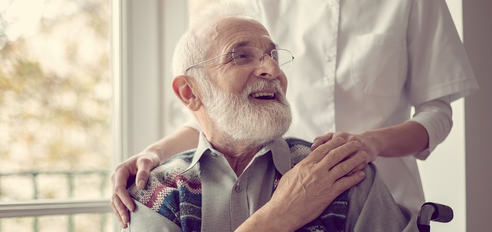 Senior man on a wheelchair, holding nurse's hand