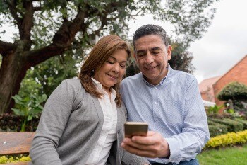 Couple sitting on a bench at the park looking at a cell phone